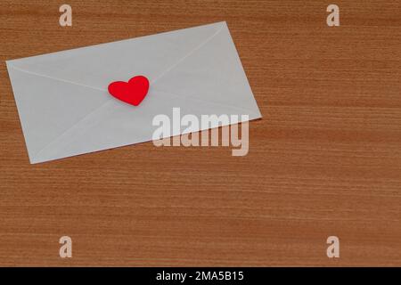 Liebesbrief zum Valentinstag in einem weißen Umschlag, verschlossen und versiegelt mit einem roten Herz auf einem hölzernen Hintergrund von einem Liebhaber. Stockfoto