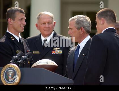 050420-N-0000A-002. [Complete] Szene Caption: US Navy Academy (USNA) Midshipman First Class (MIDN 1/C) Josh Smith (links) präsentiert US-Präsident George W. Bush einen Fußball bei der Präsentation der Trophäe des Oberbefehlshabers an Mitglieder des USNA-Fußballteams in einer Zeremonie im White House Rose Garden. Hinter MIDN 1/C Smith steht USN Vice Admiral (VADM) Rodney P. Rempt, Superintendent der US Naval Academy, und rechts neben dem Präsidenten befindet sich MIDN 1/C Aaron Polanco, Team Quarterback. Präsident Bush gratulierte dem Team zum zweiten Mal in Folge zum Sieg der Trophäe des Oberbefehlshabers. Stockfoto