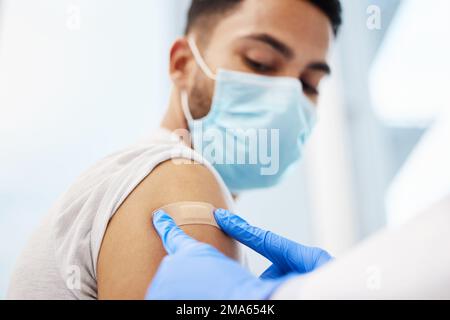 So, fertig. Eine nicht erkennbare Ärztin, die ihrem Patienten ein Pflaster anlegte, nachdem sie ihm den Covid-Impfstoff gegeben hatte. Stockfoto
