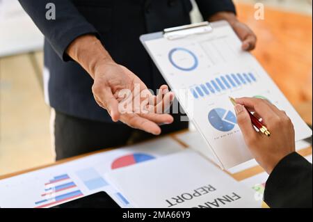 Professioneller asiatischer Geschäftsmann oder männlicher Finanzanalyst, der seine Idee mit seinen Kollegen diskutiert und teilt und gemeinsam an einem Finanzbericht arbeitet. Freistellen Stockfoto