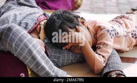 Süßes indisches Baby schläft friedlich im Bett mit ihrer Mutter zu Hause. 5-jährige unschuldige Tochter umarmt und lacht, während sie auf dem gestreiften Bett liegt. Ein Bisschen Stockfoto