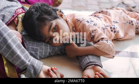 Süßes indisches Baby schläft friedlich im Bett mit ihrer Mutter zu Hause. 5-jährige unschuldige Tochter umarmt und lacht, während sie auf dem gestreiften Bett liegt. Ein Bisschen Stockfoto