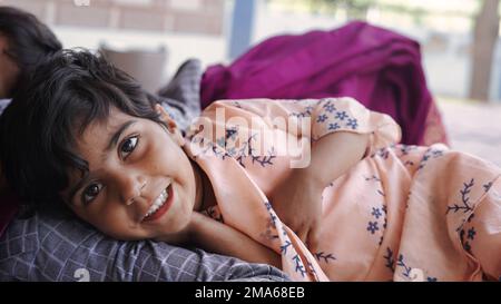 Süßes indisches Baby schläft friedlich im Bett mit ihrer Mutter zu Hause. 5-jährige unschuldige Tochter umarmt und lacht, während sie auf dem gestreiften Bett liegt. Ein Bisschen Stockfoto