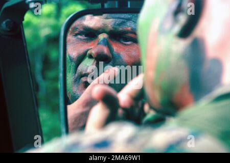 US Marine Corps (USMC) STAFF Sergeant (SSGT) Michael G. Walker, WARTUNGSLEITER der Motor Transport Company (MTS), Hauptquartier Bataillon, 3. Marine Division, trägt Tarnfarbe auf, bevor er an einer Feldübung für den Heckbereich im Central Training Area (CTA) in Okinawa, Japan teilnimmt. Basis: CTA Okinawa Land: Japan (JPN) Stockfoto