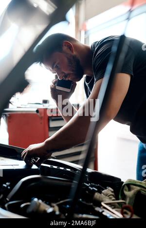 Ich habe das Problem gefunden. Ein Mechaniker, der mit seinem Handy spricht, während er in einer Autowerkstatt arbeitet. Stockfoto