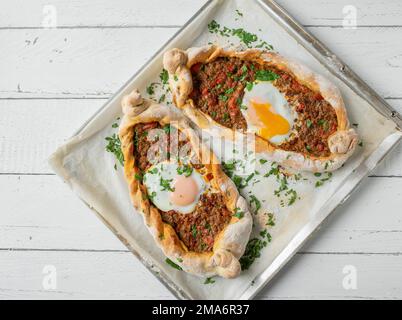 Türkische Pide mit würziger Hackfleischfüllung und pochierter Eiergarnierung auf einem Hintergrund isoliert auf weißem Hintergrund. Flach verlegt Stockfoto