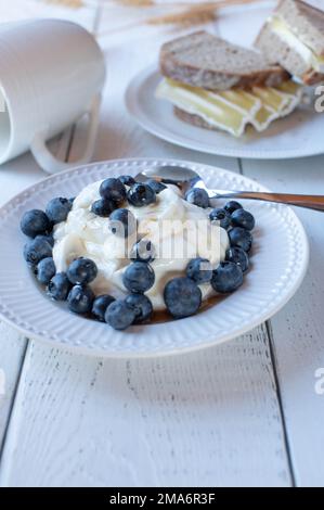 Proteinfrühstück für Muskelbau mit griechischem Joghurt, frischen Biersorten und Ahornsirup. Serviert mit einem Roggenbrot-Sandwich und fettarmem Quark-Käse Stockfoto