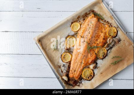 Im Ofen gebackener halber Lachs gefüllt mit Zitronen-, Knoblauch- und Thymian-Marinade auf einem Backblech auf weißem Hintergrund mit Platz für Text. Flach verlegt Stockfoto