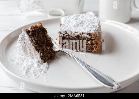 Italienische Schokolade, Mandelkuchen, Torta Caprese, serviert auf einem weißen Teller mit Gabel. Nahaufnahme und Vorderansicht Stockfoto