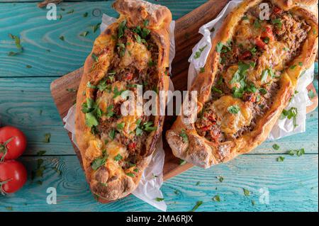 Türkische Pide mit Rinderhack, Gemüse und Käse auf einem Holztisch. Flach verlegt Stockfoto