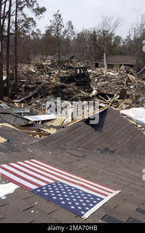 Eine amerikanische Flagge sitzt auf dem Dach eines schwer beschädigten Hauses, während US Army (USA) National Guardsman SPECIALIST (SPC) James Meidl Trümmer in Pass Christian, Mississippi (MS) mit einem D-7-Bulldozer entfernt, um die Hilfsmaßnahmen für den Hurrikan Katrina zu unterstützen. Basis: Pass Christian State: Mississippi (MS) Land: Vereinigte Staaten von Amerika (USA) Stockfoto