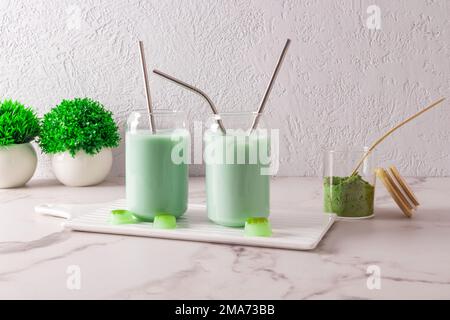 Zwei moderne Gläser in Form einer Bierdose mit Teematcha mit Stroh auf einem Brett an einer grauen Wand. Eine Alternative zum Kaffee. Koffein Stockfoto
