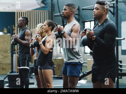 Die Kugelhantel ist ein effektives Gewicht, um Muskeln zu stärken. Eine Gruppe sportlicher junger Leute, die in einem Fitnessraum mit Kugelhanteln trainieren. Stockfoto