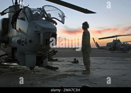 Ein Marine des US Marine Corps (USMC) steht neben einem geparkten USMC AH-1W Super Cobra Helicopter, Marine Light Attack Helicopter Squadron 369 (HML/A-369), in Forward Operation Base (FOB) Al Qaim, Al Anbar Province, Irak. HML/A-369 befindet sich im Irak, um Lufteinsätze zur Aufstandsbekämpfung zur Unterstützung der IRAKISCHEN FREIHEIT durchzuführen. Basis: Al-Qaim-Staat: Al-Anbar-Land: Irak (IRQ) Stockfoto