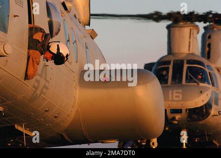 Besatzungsmitglied des US Marine Corps (USMC) eines USMC CH-46E Sea Knight Hubschraubers, Marine Medium Helicopter Squadron 166 (HMM-166), Sea Elks, Marine Corps Air Station (MCAS) Miramar, Kalifornien (CA), Er rammt aus dem Fenster seines Hubschraubers und überprüft die vertikale Entfernung, während er sich auf dem Flugdeck des Tarawa Class Amphibious Assault Ship USS PELELIU (LHA 5) der US Navy (USN) befindet. Das PELELIU, das Flaggschiff der Expeditionary Strike Group (ESG) 3, befindet sich vor der Küste Südkaliforniens im Rahmen der Composite Unit Training (COMPTUEX) in Vorbereitung auf seinen bevorstehenden sechsmonatigen Einsatz zur Unterstützung der Stockfoto