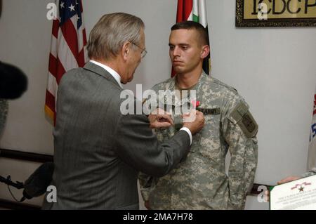 051224-N-0696M-275. [Complete] Scene Caption: The Honorable Donald H. Rumsfeld (links), USA US-Verteidigungsminister (SECDEF), überreicht die Bronze Star Medaille an die USA Army SPC. Lucas Crowe, 2. Bataillon, 1. Infanterie-Regiment, Multinationale Streitkräfte-Nordwest, bei Forward Operating Base (FOB) Courage, Mosul, Provinz Ninawa, Irak, am 24. Dezember, 2005. SPEZIALIST Crowe erhält diese Auszeichnung für seine Handlungen am 15. Dezember 2005, als er das Leben eines zweijährigen Irakers aus einem überfluteten Keller rettete. Er führte eine Herz-Lungen-Wiederbelebung durch, belebte den Jungen und tröstete ihn, bis medizinische Hilfe eintraf. Der SECDEF befindet sich im Land Stockfoto