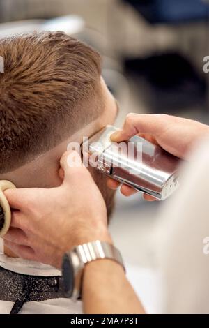 Friseur trimmt Haare mit Haarschneider an einem gutaussehenden bärtigen Mann Stockfoto
