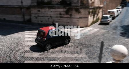 Ein Smart-Auto, das auf den Kopfsteinpflasterstraßen Roms und Italiens über eine Fußgängerüberquerung fährt. Stockfoto