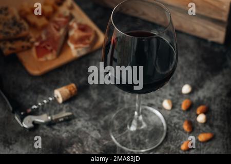 Rotwein im Glas. Ein Glas Rotwein liegt auf dem Tisch. Prosciutto mit Käse, Rotwein, Baguette, Nüssen. Rotwein mit traditionellem mediterranen Snack Stockfoto