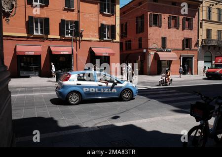 Der italienische Polizeiwagen und das Motorrad warten an einer Kreuzung in Bologna Norditalien, während eine Dame überquert. Stockfoto