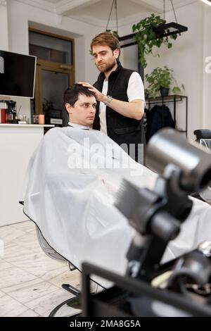 Friseurin, der gutaussehenden Mann im Friseursalon bedient. Stockfoto