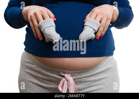 Nahaufnahme einer schwangeren Frau mit einem Paar Babysocken auf weißem Studiohintergrund als Kleidungskonzept Stockfoto