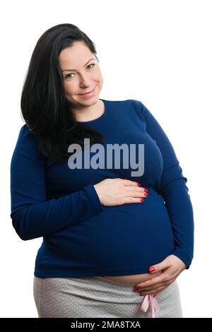 Fröhliche lächelnde zukünftige Mutter, die ihren großen Bauch hält, während sich das neun Monate andauende Schwangerschaftskonzept auf weißem Studiohintergrund isoliert Stockfoto