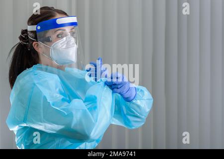 Die Krankenschwester zieht ihre Schutzhandschuhe an, während sie eine N95-Maske mit Gesichtsschutz im Gesicht trägt Stockfoto