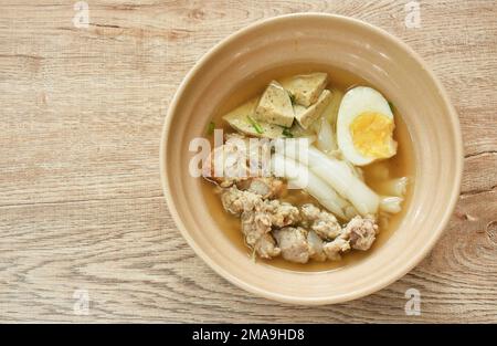 Große Reisnudeln, Wurstscheiben mit Kotelett und knusprigem Schweinefleisch, das weich gekochtes Ei in Suppe auf Schüssel serviert Stockfoto