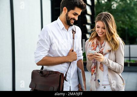 Glückliche junge Geschäftsleute, die im Freien chatten und digitale Geräte nutzen Stockfoto