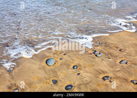 Meeresschaum am Sandstrand. Küste am Meer mit Steinen im Sand Stockfoto