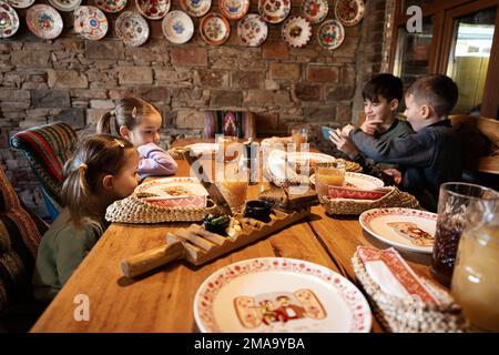 Vier Kinder sitzen in einem authentischen ukrainischen Restaurant und schauen auf Telefone. Stockfoto