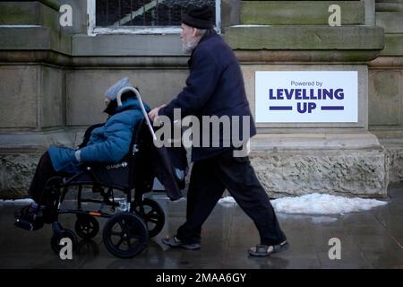 Käufer gehen vorbei an einem Schild mit der Aufschrift „Powered by Levelling Up“, das kürzlich von Premierminister Rishi Sunak und Kanzler Jeremy Hunt an der Accrington Market Hall in Lancashire angebracht wurde. Herr Sunak hat seine Entschlossenheit bekräftigt, sich zu verbessern, da die Regierung £2 Milliarden Euro für mehr als 100 Projekte im Vereinigten Königreich angekündigt hat. . Foto: Donnerstag, 19. Januar 2023. Stockfoto