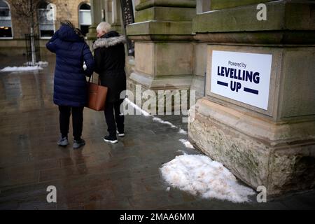 Käufer gehen vorbei an einem Schild mit der Aufschrift „Powered by Levelling Up“, das kürzlich von Premierminister Rishi Sunak und Kanzler Jeremy Hunt an der Accrington Market Hall in Lancashire angebracht wurde. Herr Sunak hat seine Entschlossenheit bekräftigt, sich zu verbessern, da die Regierung £2 Milliarden Euro für mehr als 100 Projekte im Vereinigten Königreich angekündigt hat. . Foto: Donnerstag, 19. Januar 2023. Stockfoto