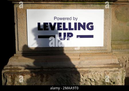 Ein Schatten einer Person auf einem Schild mit dem Aufdruck „Powered by Levelling Up“, das kürzlich von Premierminister Rishi Sunak und Kanzler Jeremy Hunt an der Accrington Market Hall in Lancashire angebracht wurde. Herr Sunak hat seine Entschlossenheit bekräftigt, sich zu verbessern, da die Regierung £2 Milliarden Euro für mehr als 100 Projekte im Vereinigten Königreich angekündigt hat. . Foto: Donnerstag, 19. Januar 2023. Stockfoto