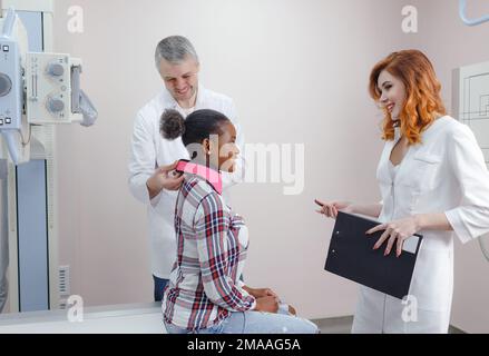 Ein Radiologe bereitet zusammen mit einer Assistentin einen afroamerikanischen Patienten auf eine Röntgenaufnahme vor Stockfoto