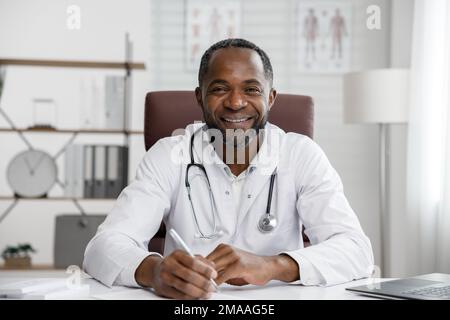 Ein afroamerikanischer Arzt begrüßt die Online-Patientenberatung auf dem Laptop. Ein Büro, das telemedizinische Dienste erbringt. Online-Medizin und Stockfoto