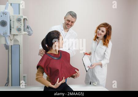 Ein männlicher Radiologe bereitet den Patienten zusammen mit einem Assistenten auf eine Röntgenaufnahme vor Stockfoto