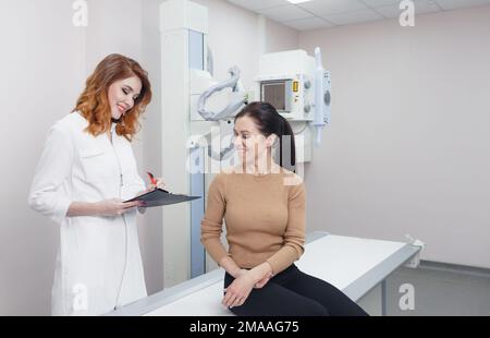 Eine Radiologin kommuniziert mit einem Patienten im Röntgenraum, bevor der Eingriff beginnt Stockfoto