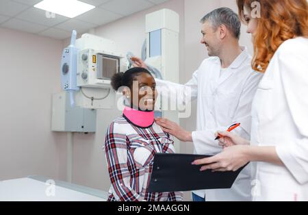 Ein Radiologe bereitet zusammen mit einer Assistentin einen afroamerikanischen Patienten auf eine Röntgenaufnahme vor Stockfoto