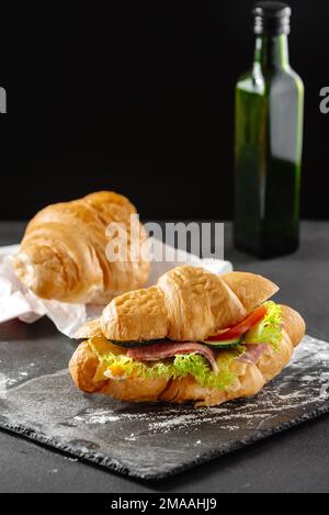 Köstliches Frühstück. Großes Croissant-Sandwich mit Wurst, Käse und Tomaten Stockfoto