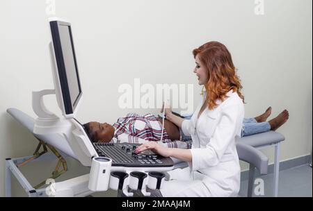 Ultraschallverfahren. Die Ärztin führt eine Ultraschalluntersuchung der Bauchhöhle eines afroamerikanischen Patienten durch. Stockfoto