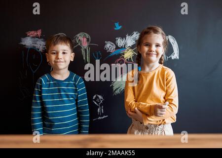 Süßes kleines Mädchen und Junge, gemalt mit Buntstift an der Wand. Kinderwerke. Süße Geschwister, die auf eine Tafel schreiben. Stockfoto