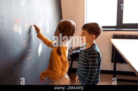 Süßes kleines Mädchen und Junge, gemalt mit Buntstift an der Wand. Kinderwerke. Süße Geschwister, die auf eine Tafel schreiben. Stockfoto