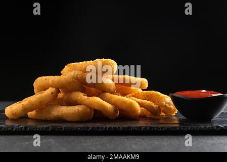 Calamari-Ringe frittiert in Panade. Knusprige Tintenfischringe auf dunklem Hintergrund mit Sauce. Stockfoto