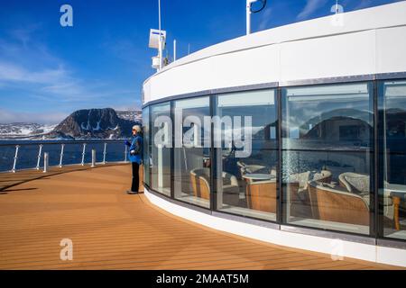 Touristisches Mädchen, das sich auf dem Hauptdeck des Expeditionsschiffs Greg Mortimer in Svalbard-Inselgruppe, arktisches Norwegen, erholt. Stockfoto