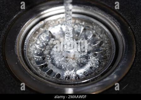 Das Wasser fällt vom Wasserhahn zum rostfreien Waschbecken und fließt hinunter zum Wasserloch, Getränkekonzept Stockfoto