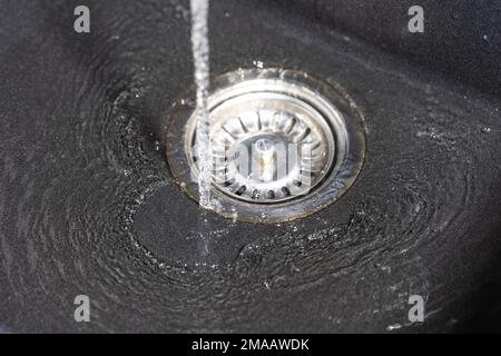 Das Wasser fällt vom Wasserhahn zum rostfreien Waschbecken und fließt hinunter zum Wasserloch, Getränkekonzept Stockfoto