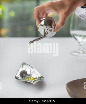 Detail einer Person, die Olivenöl über eine Metallschüssel gießt. Konzept der Haute Cuisine und Gourmetprodukte. mittelmeererzeugnisse. Gesundes Essen. Stockfoto