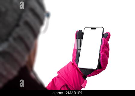 Mädchen hält ein Handy in Skiausrüstung. Pinke Winterjacke mit Handschuhen und Hut. Konzept der Telefonbenutzung auf einer Skipiste; isoliertes Display und Backgrou Stockfoto